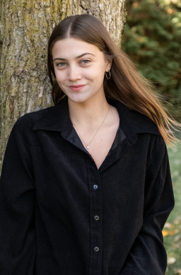 A white feamle with long brown hair wearing a black button-down top. She is looking directly at the camera and smiling. 