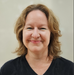 A white female with shoulder length light brown hair, wearing a black v-neck top. She is looking directly at the camera with a big smile.