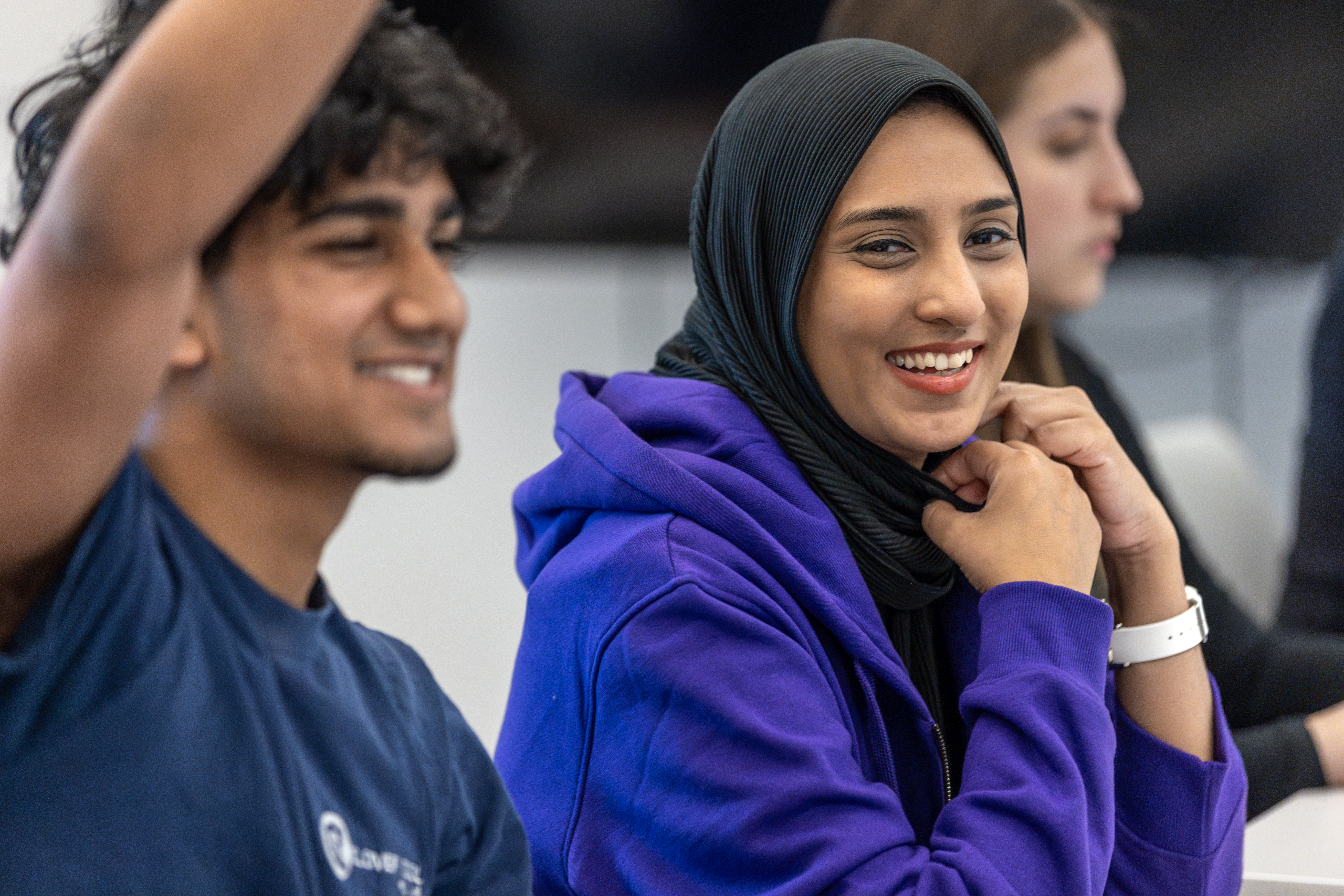 students in a classroom participating, smiling, and raising hands